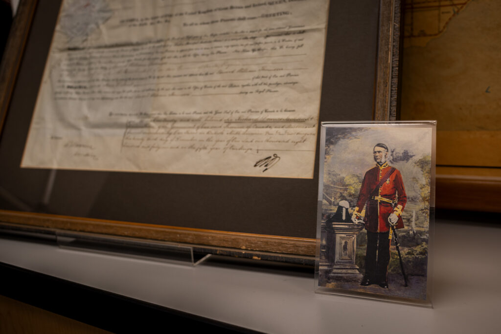 A photograph of a portrait of Edward William Thomson with his commission document from Queen Victoria in the background.